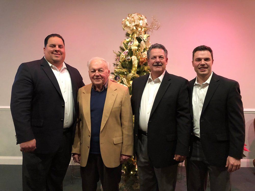 Four men in suits are posing for a picture in front of a christmas tree.