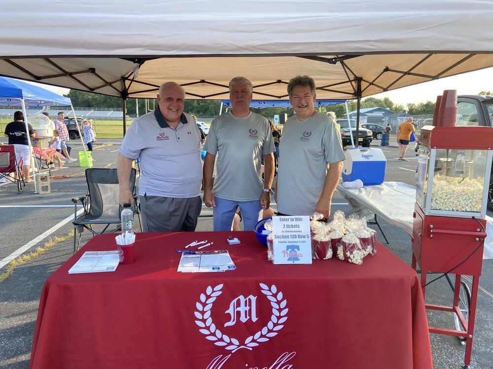 Three men are standing in front of a table with a popcorn machine.