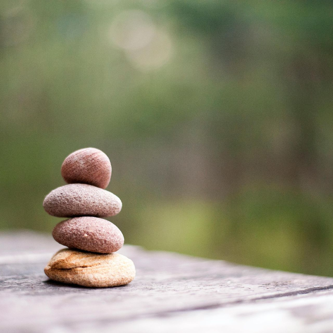 Four stacked stones, balanced atop a weathered wood surface, with a blurry green background.