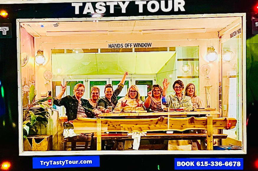 A group of people are posing for a picture in front of a sign that says tasty tour.