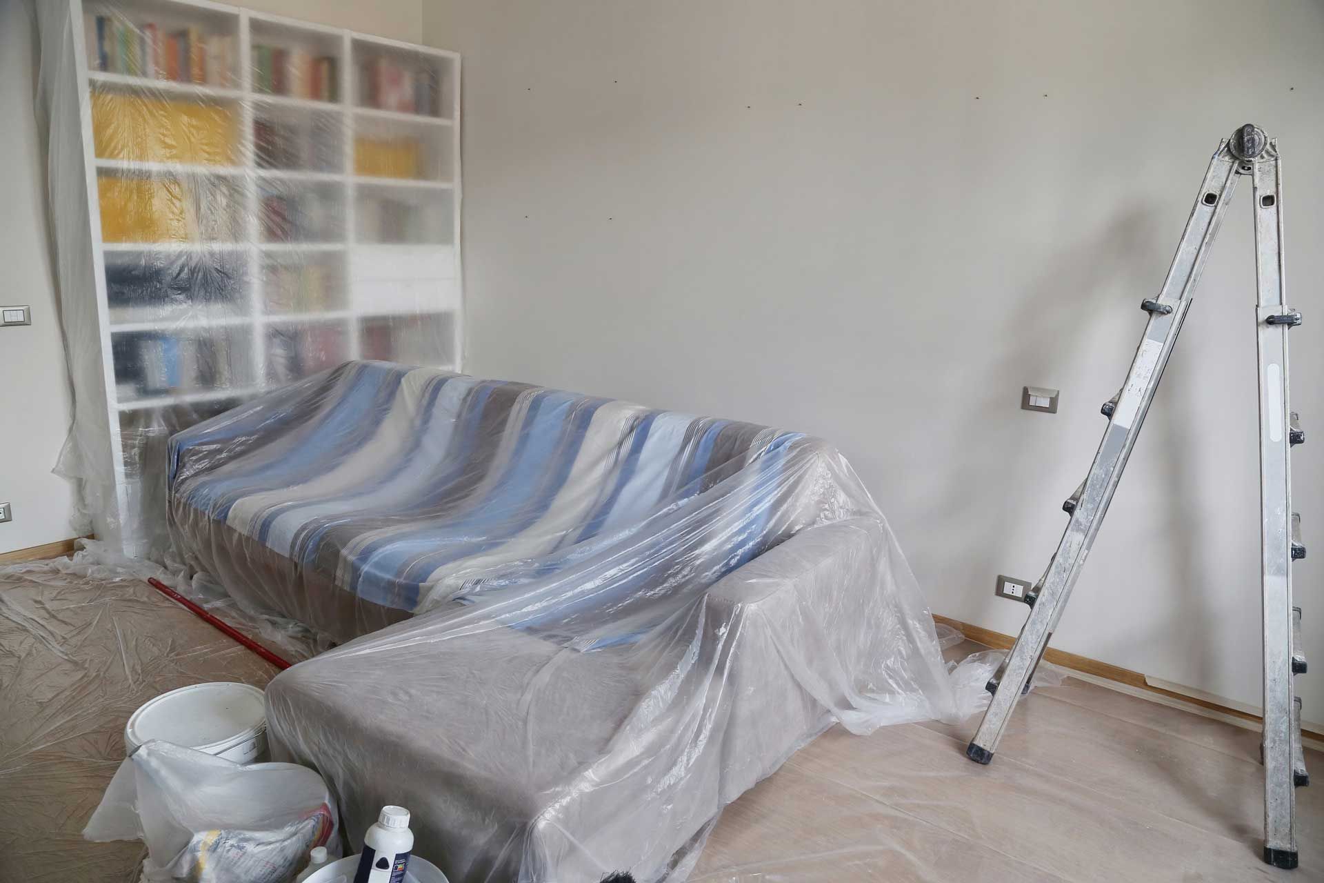 A living room with a couch covered in plastic and a ladder.
