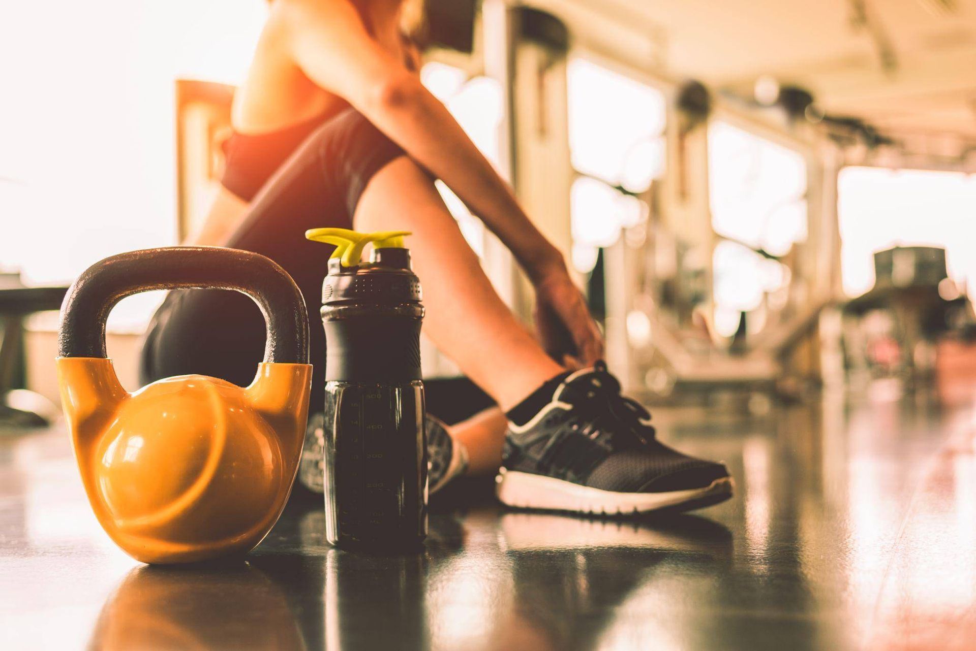 A woman is sitting on the floor in a gym tying her shoes.