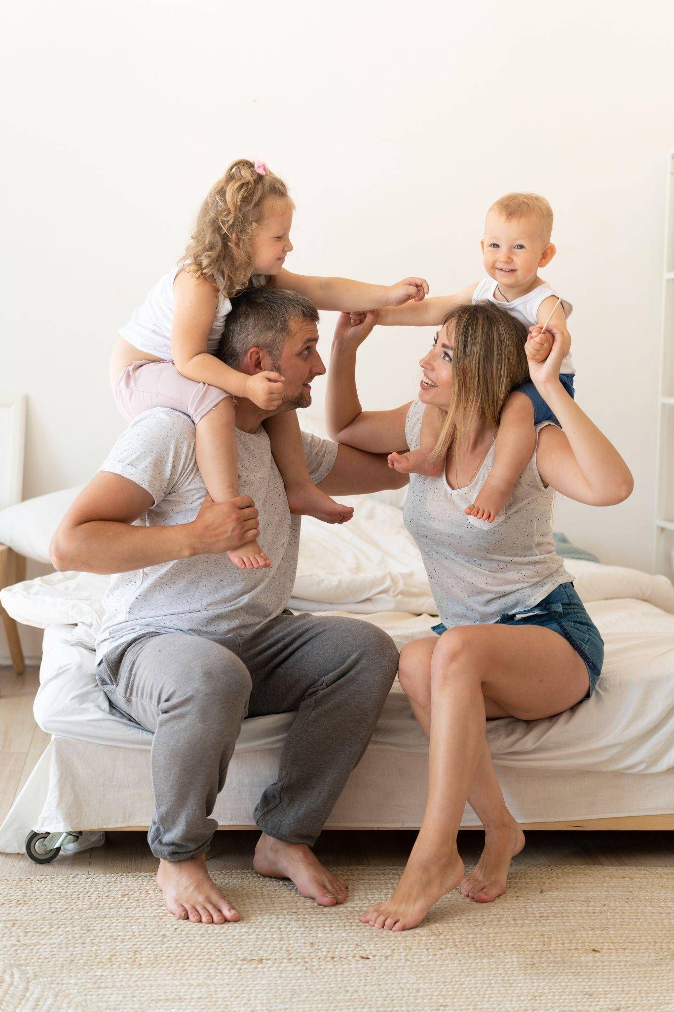 A family is sitting on a bed with two children on their shoulders.