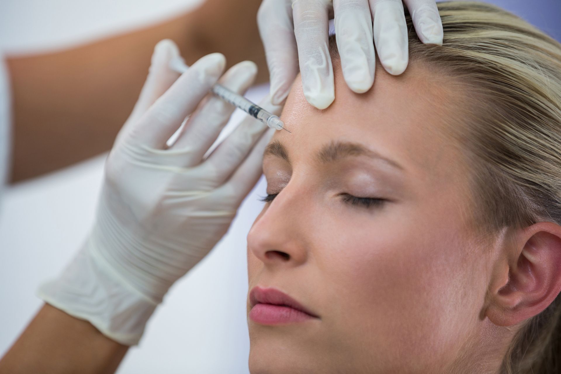 A woman is getting a botox injection in her forehead.