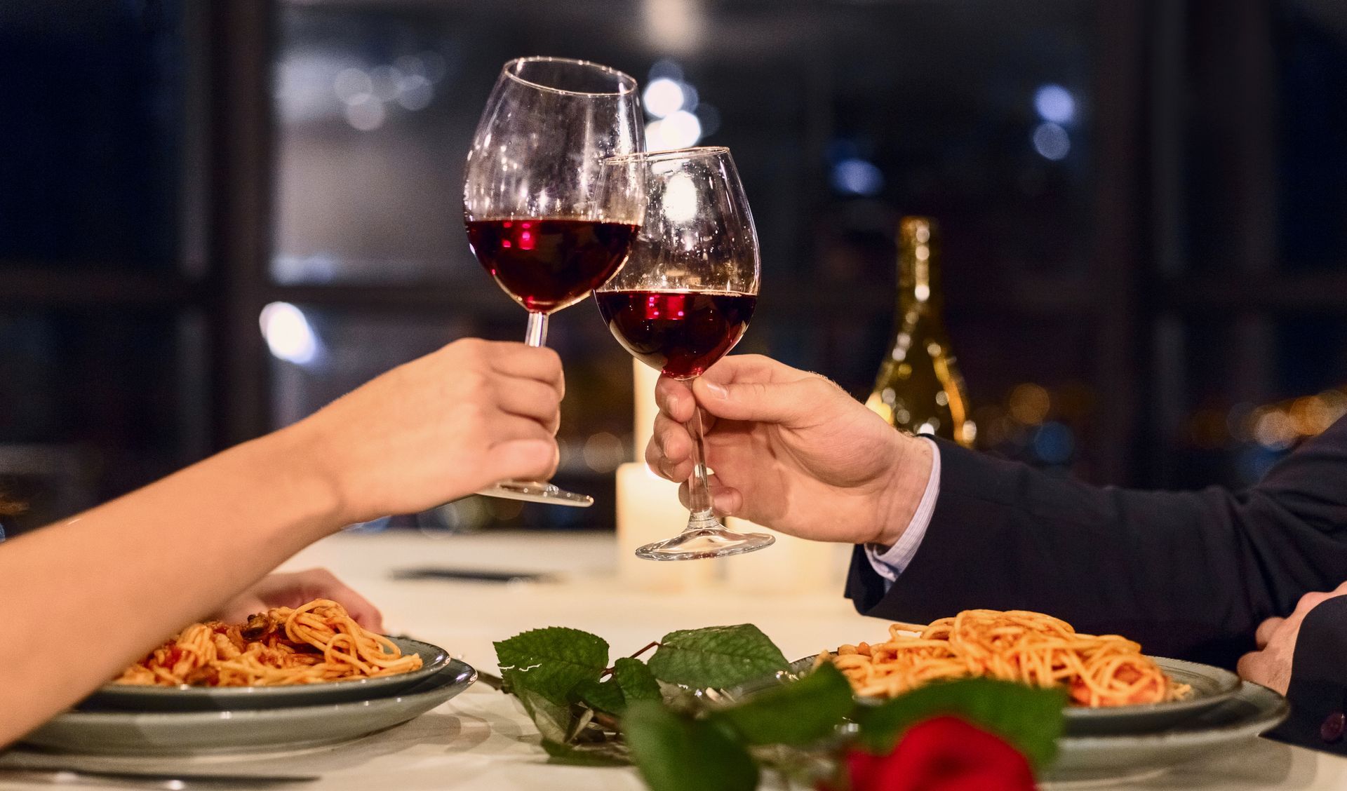 A man and a woman are toasting with wine glasses at a dinner table.