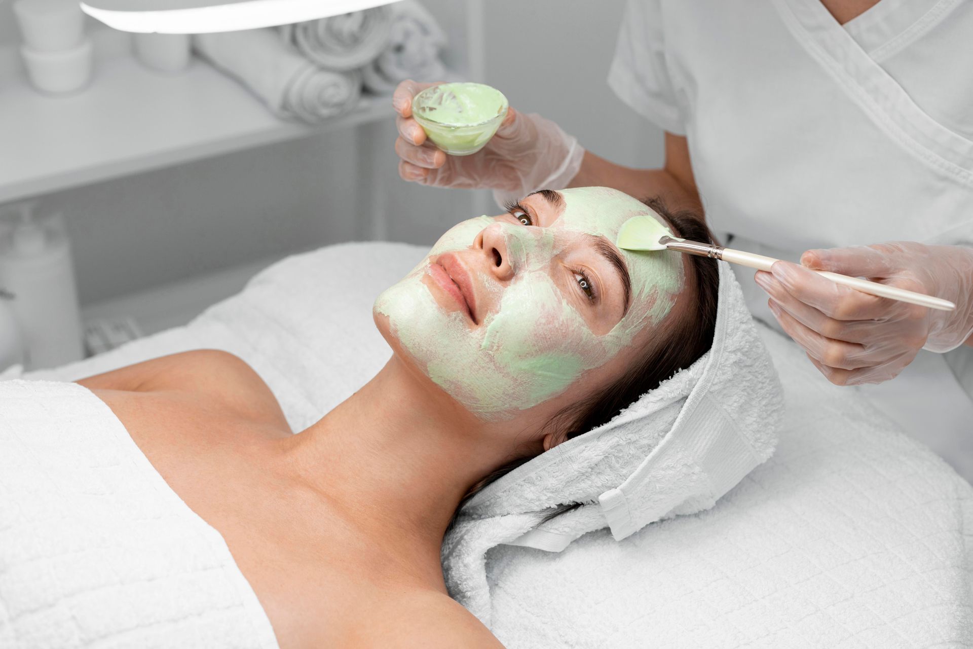 A woman is getting a green mask on her face at a spa.
