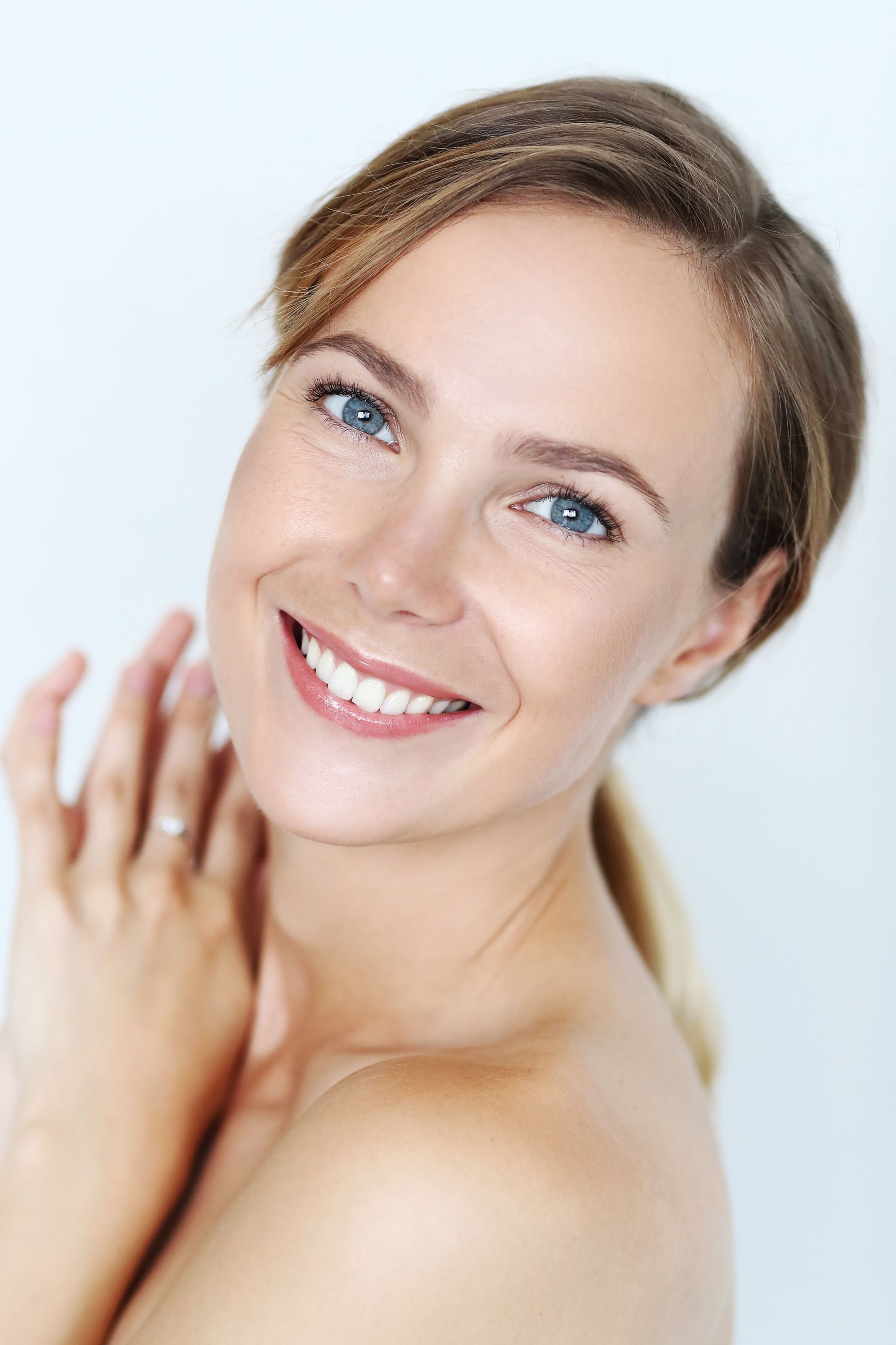 A woman is smiling and touching her face with her hands.