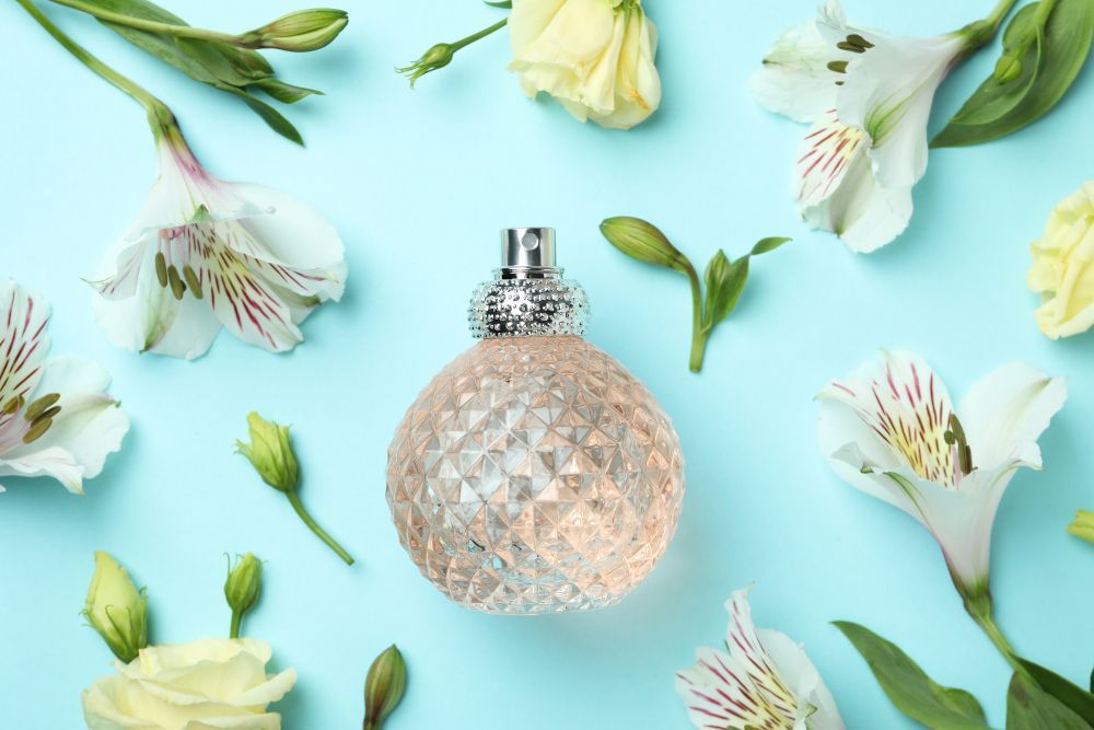 A bottle of perfume surrounded by flowers on a blue background.