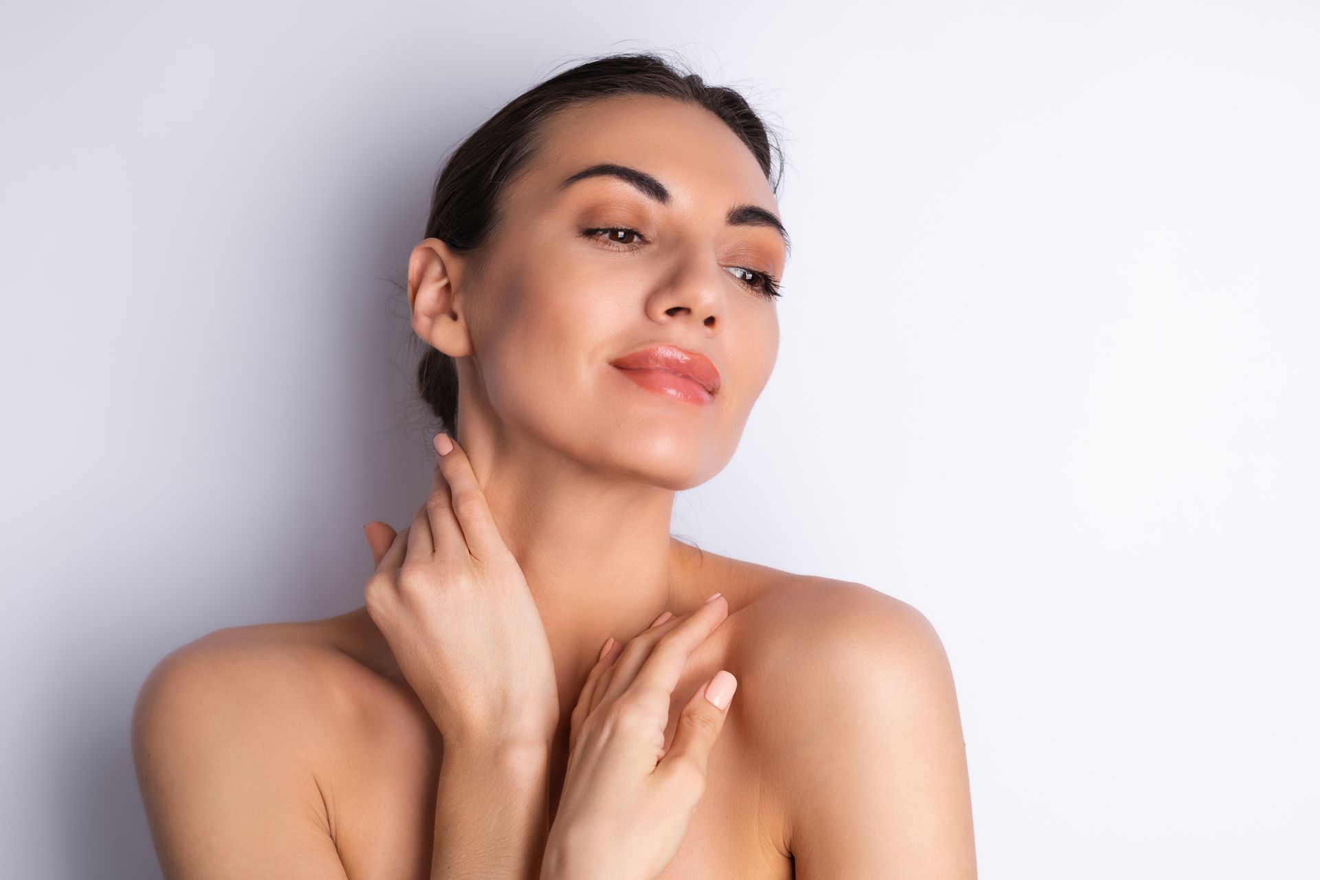 A woman is touching her neck with her hands and smiling.