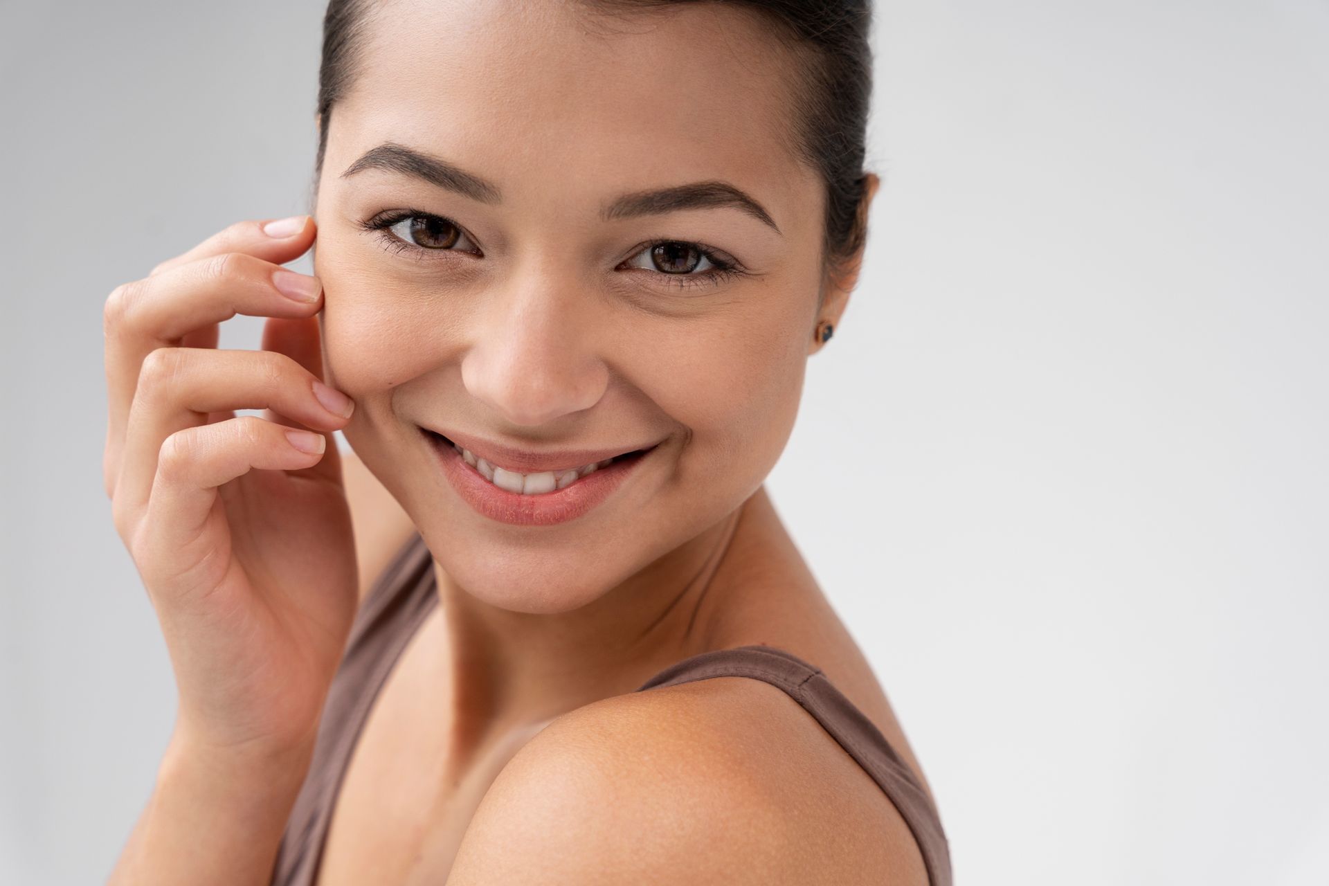 A woman is smiling and touching her face with her hand.