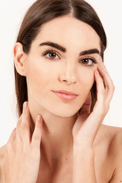 A woman is touching her face with her hands and smiling.