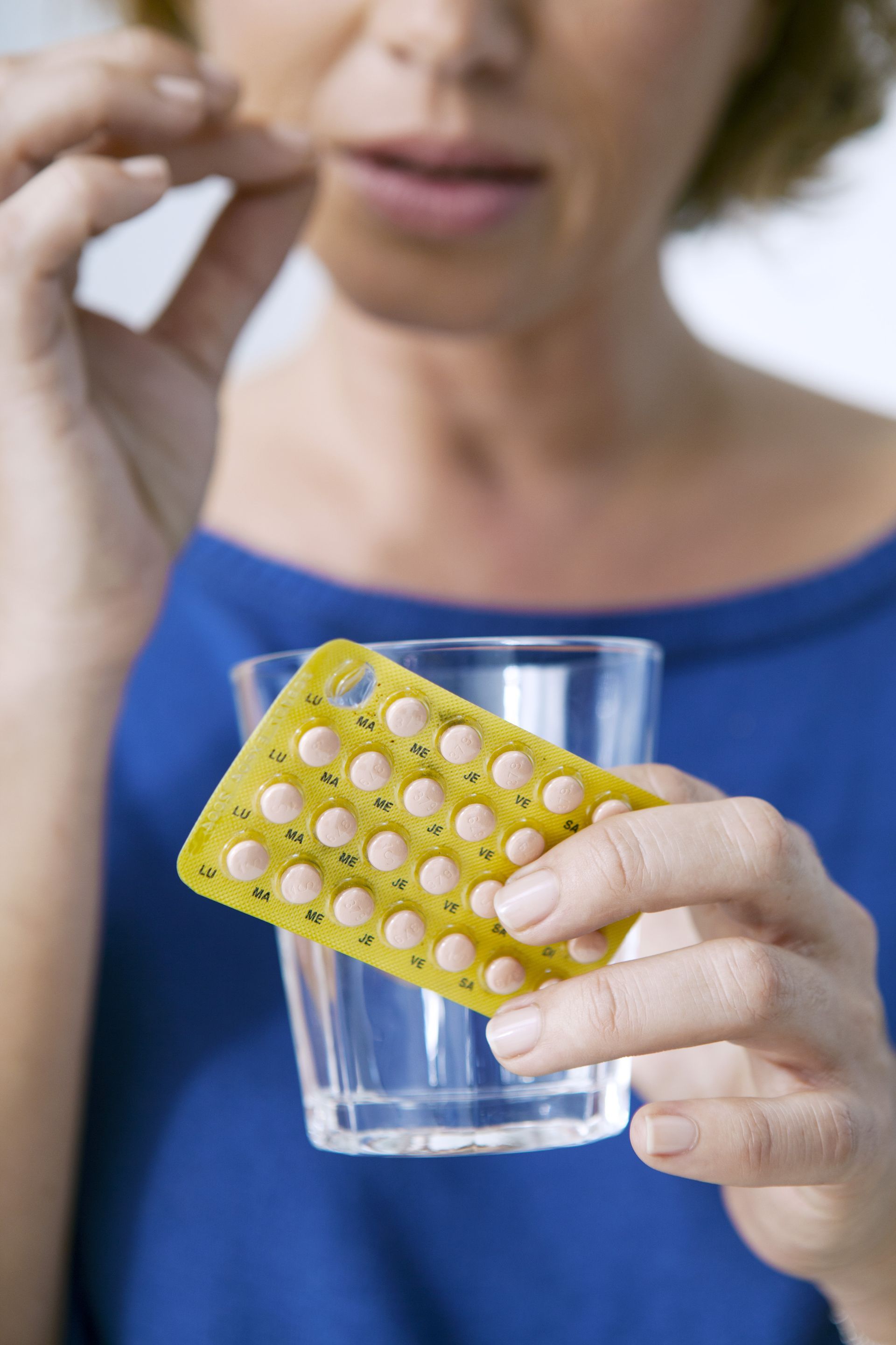 A woman is holding a pack of pills and a glass of water.