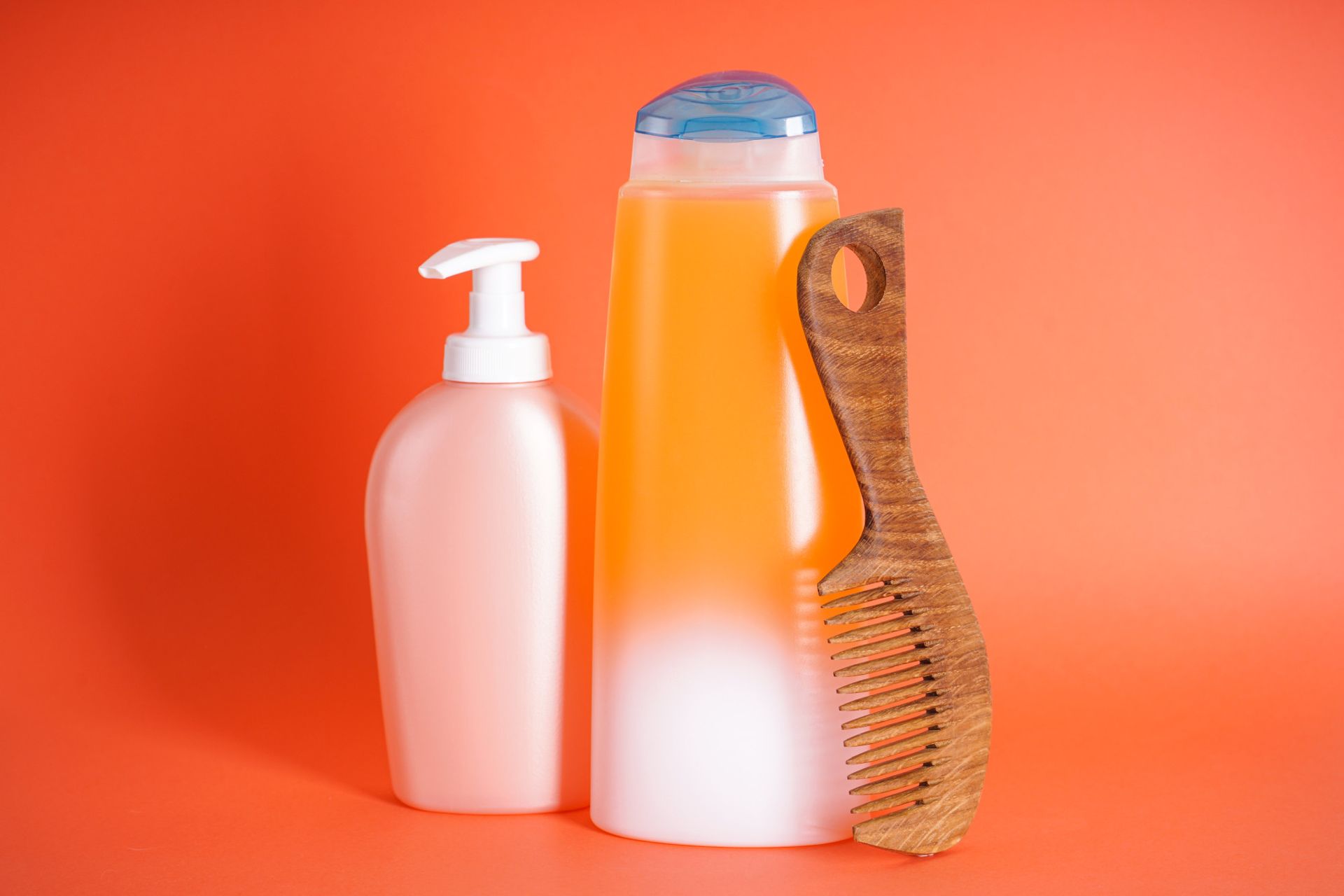 A bottle of shampoo , a bottle of lotion and a wooden comb on an orange background.