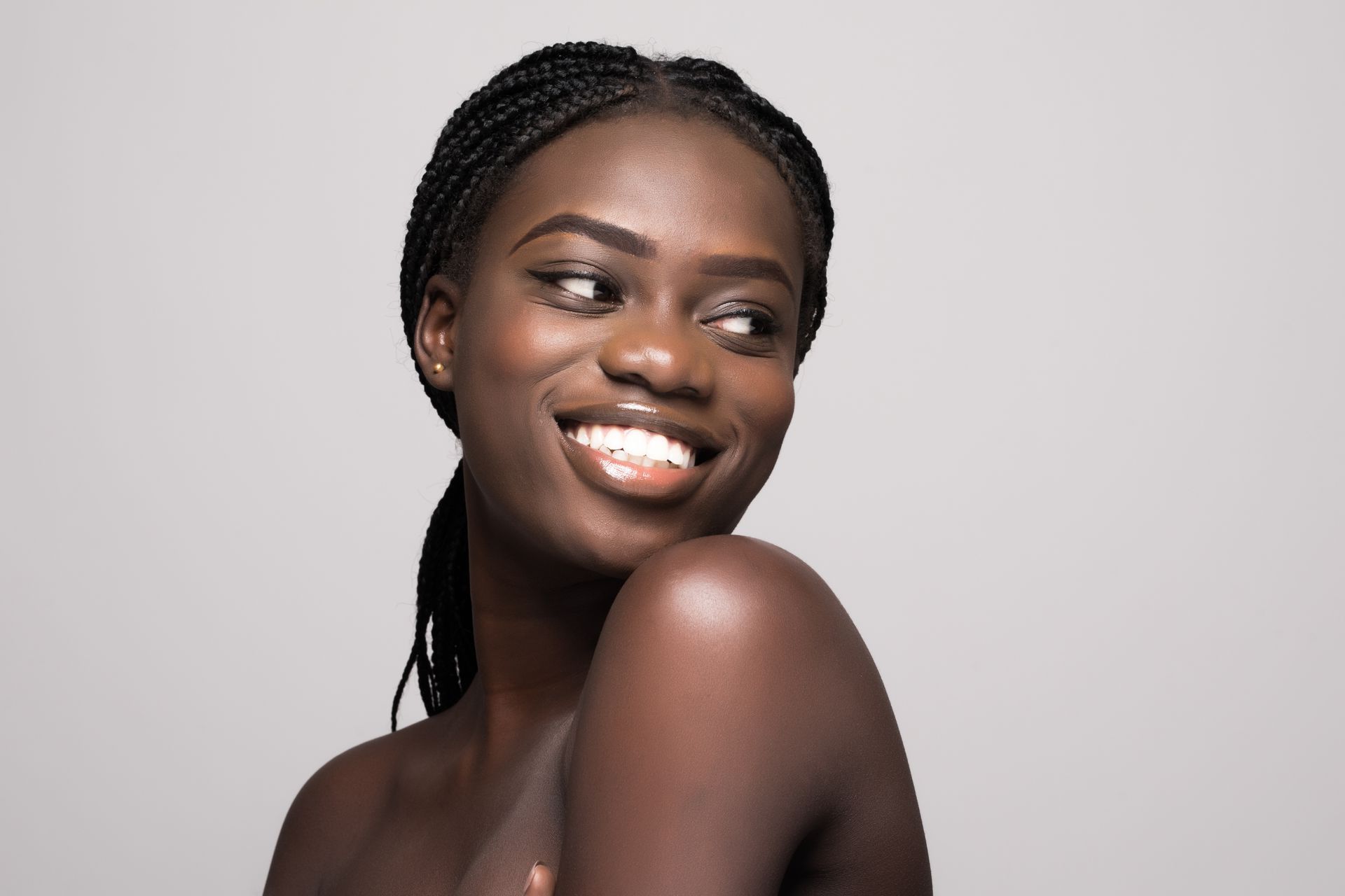 A woman with braids is smiling and looking over her shoulder.