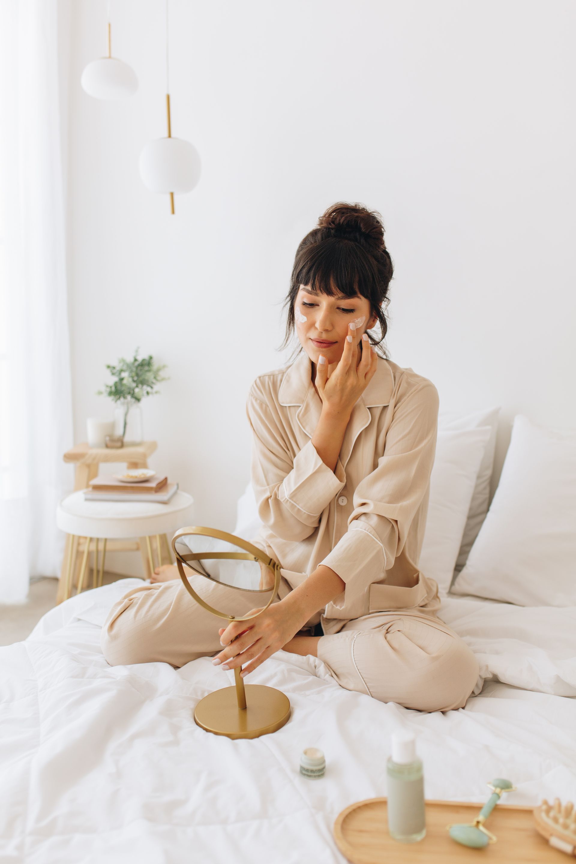 A woman is sitting on a bed looking at her face in a mirror.