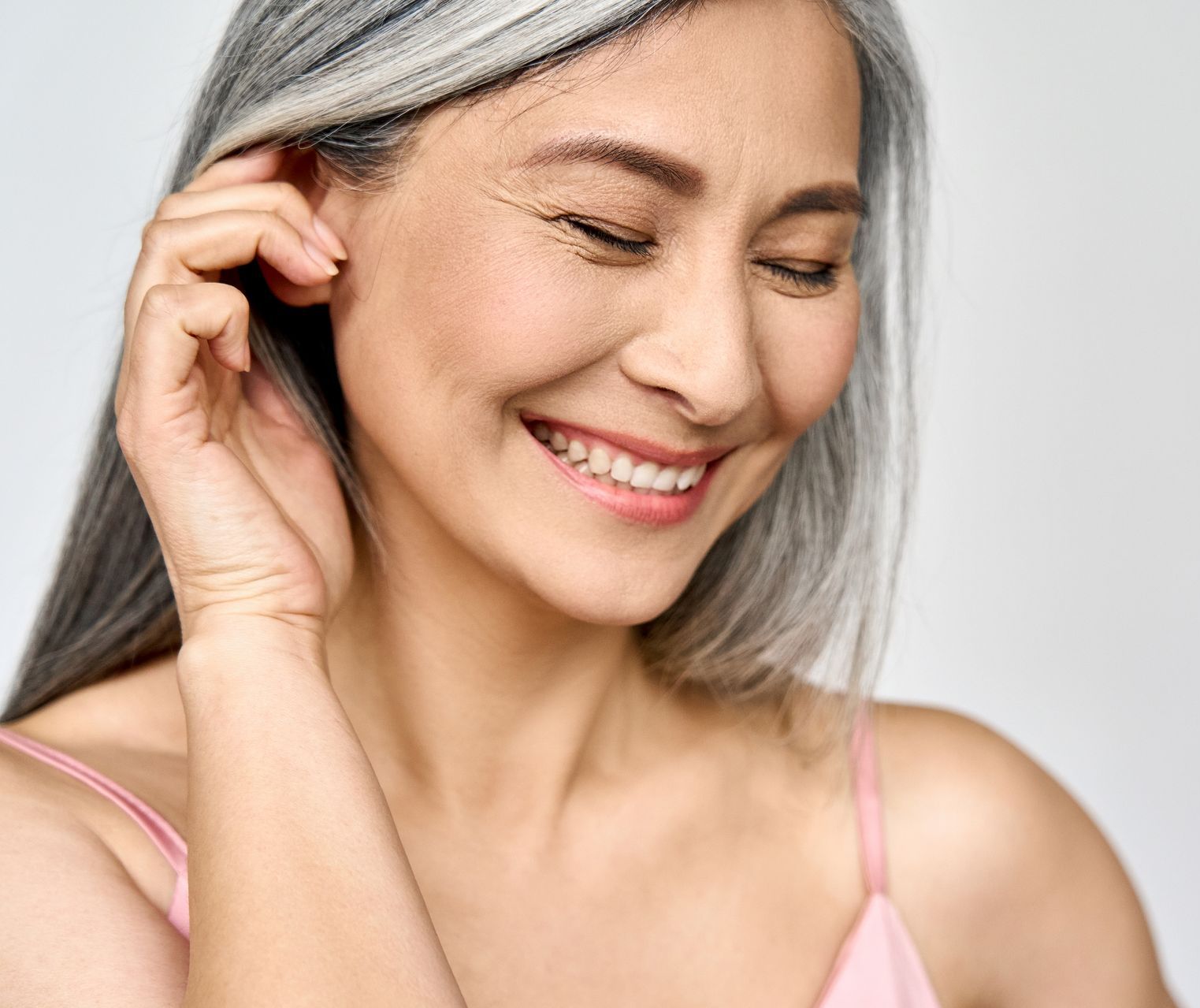 A woman with gray hair is smiling and touching her ear.