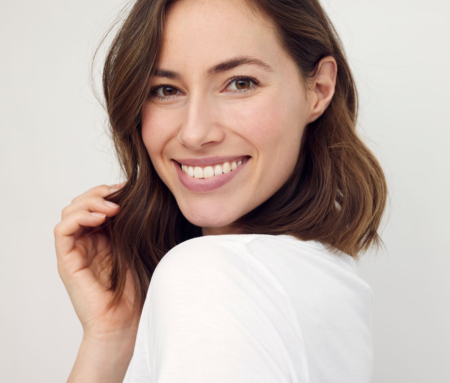 A woman in a white shirt is smiling and looking over her shoulder