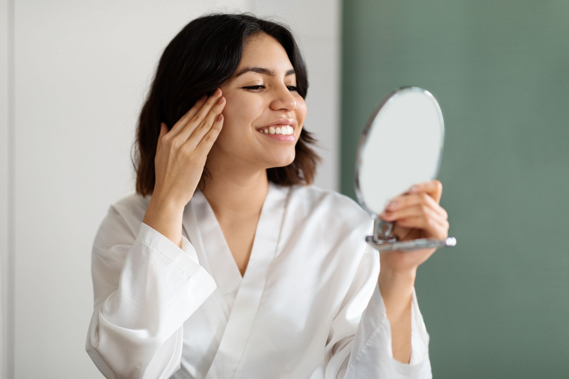 A woman is smiling while looking at her face in a mirror.