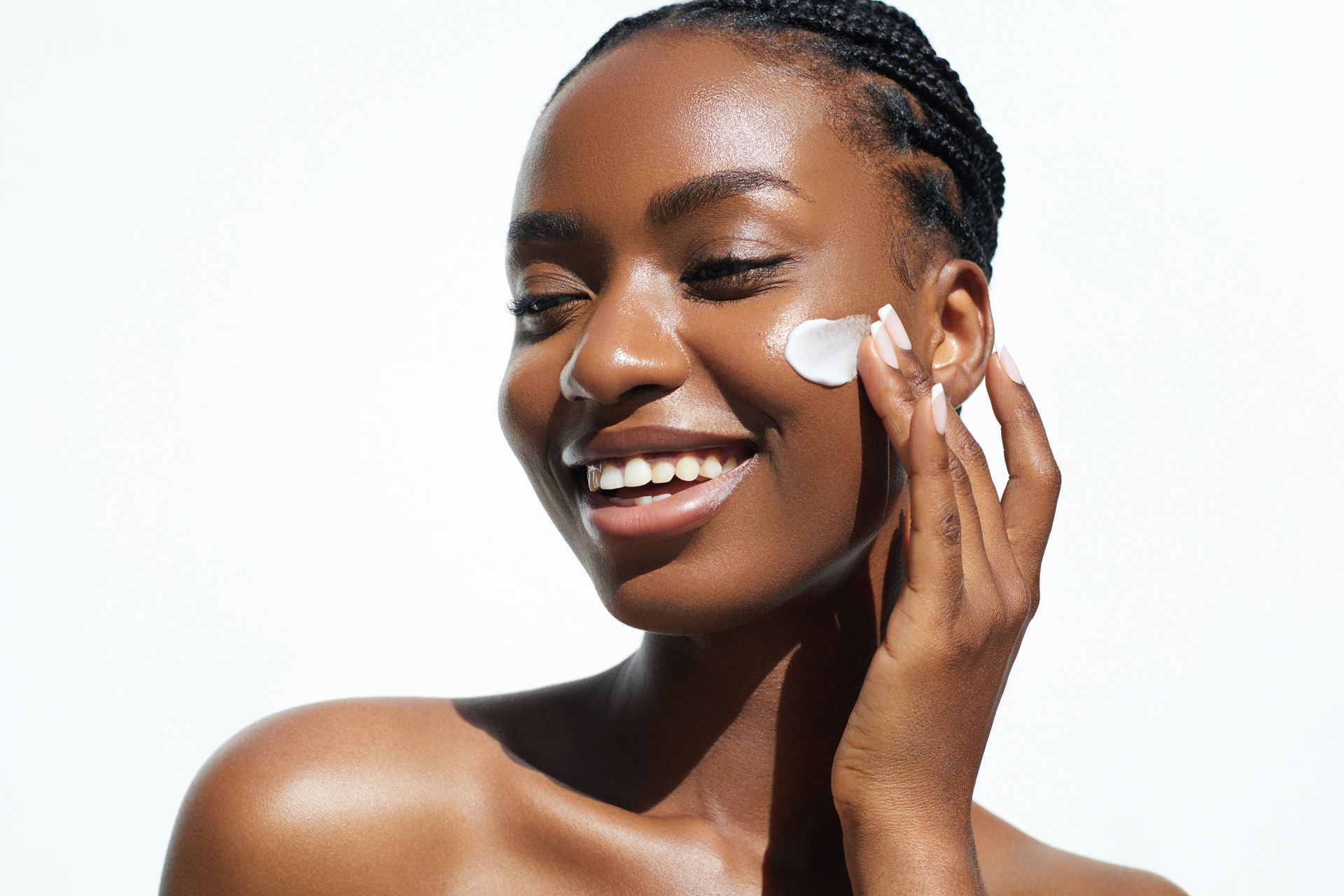 A woman is smiling while applying cream to her face.