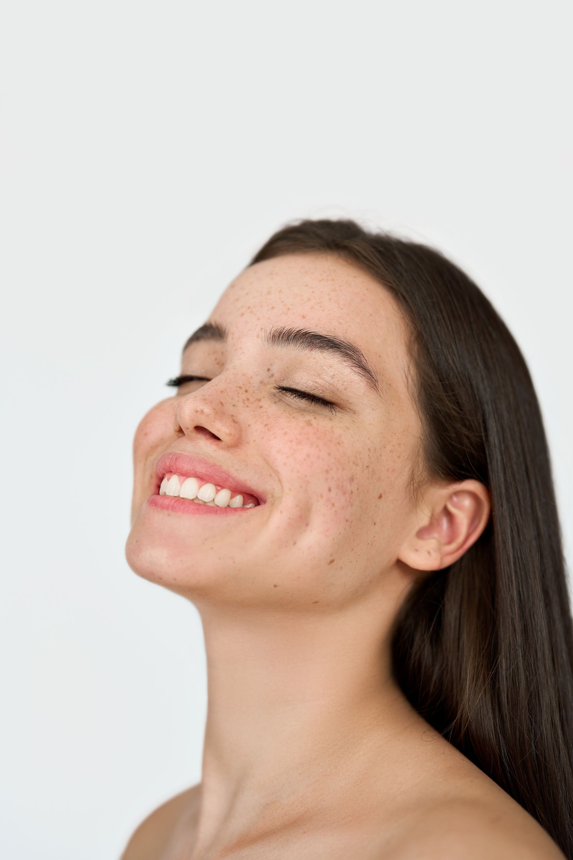 A woman with freckles is smiling with her eyes closed.