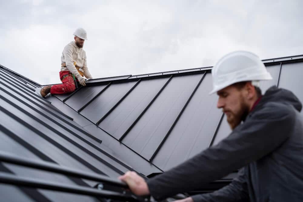 Roofer in orange hard hat, hammers metal flashing on a white commercial roof.