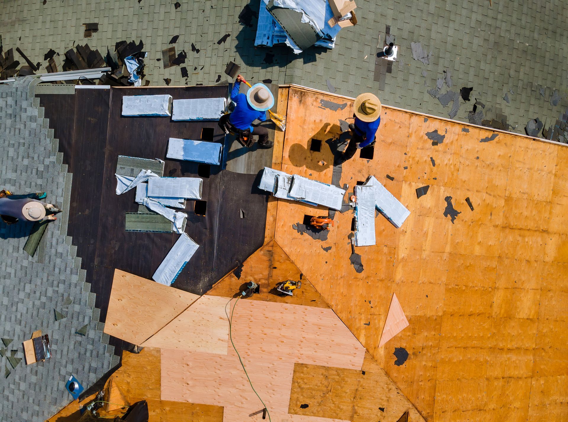 Construction worker on rooftop using a drill. He wears a white vest, hard hat, and holds a power tool.