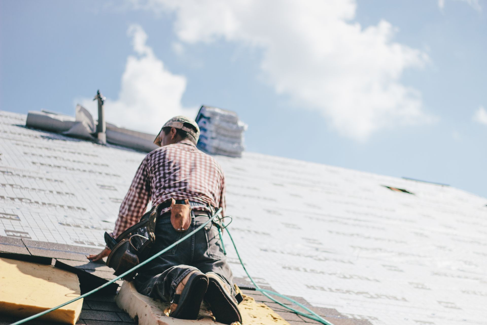 Person on ladder repairing roof of a house, surrounded by autumn trees under a blue sky.