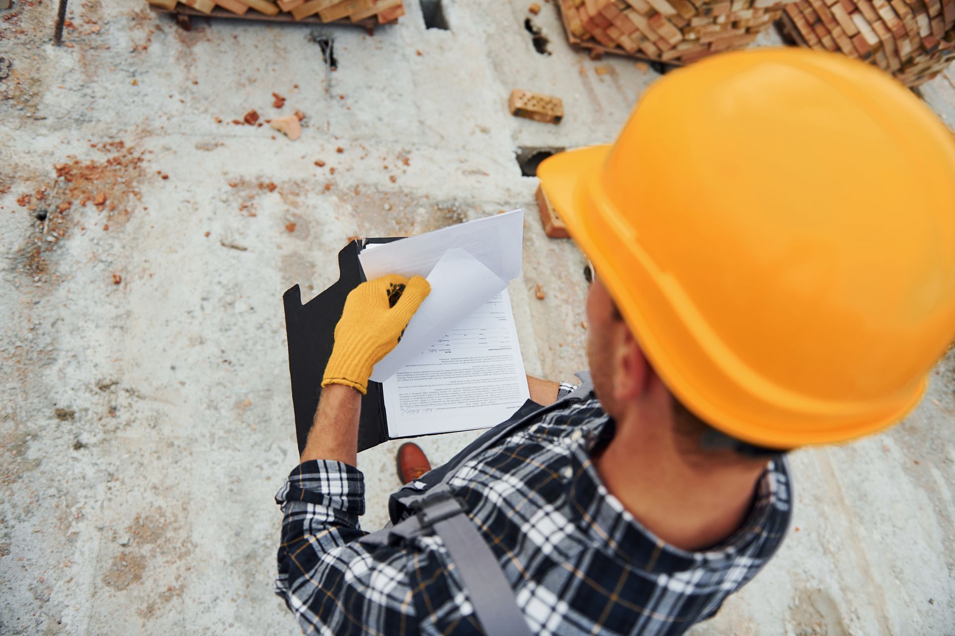 Construction worker with tablet smiles, flanked by colleagues on a rooftop, studying blueprints.