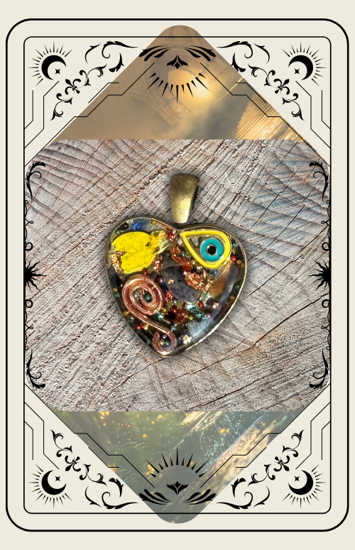 A heart-shaped pendant with mixed media, including a small yellow eye charm and copper coils, set on a textured surface.