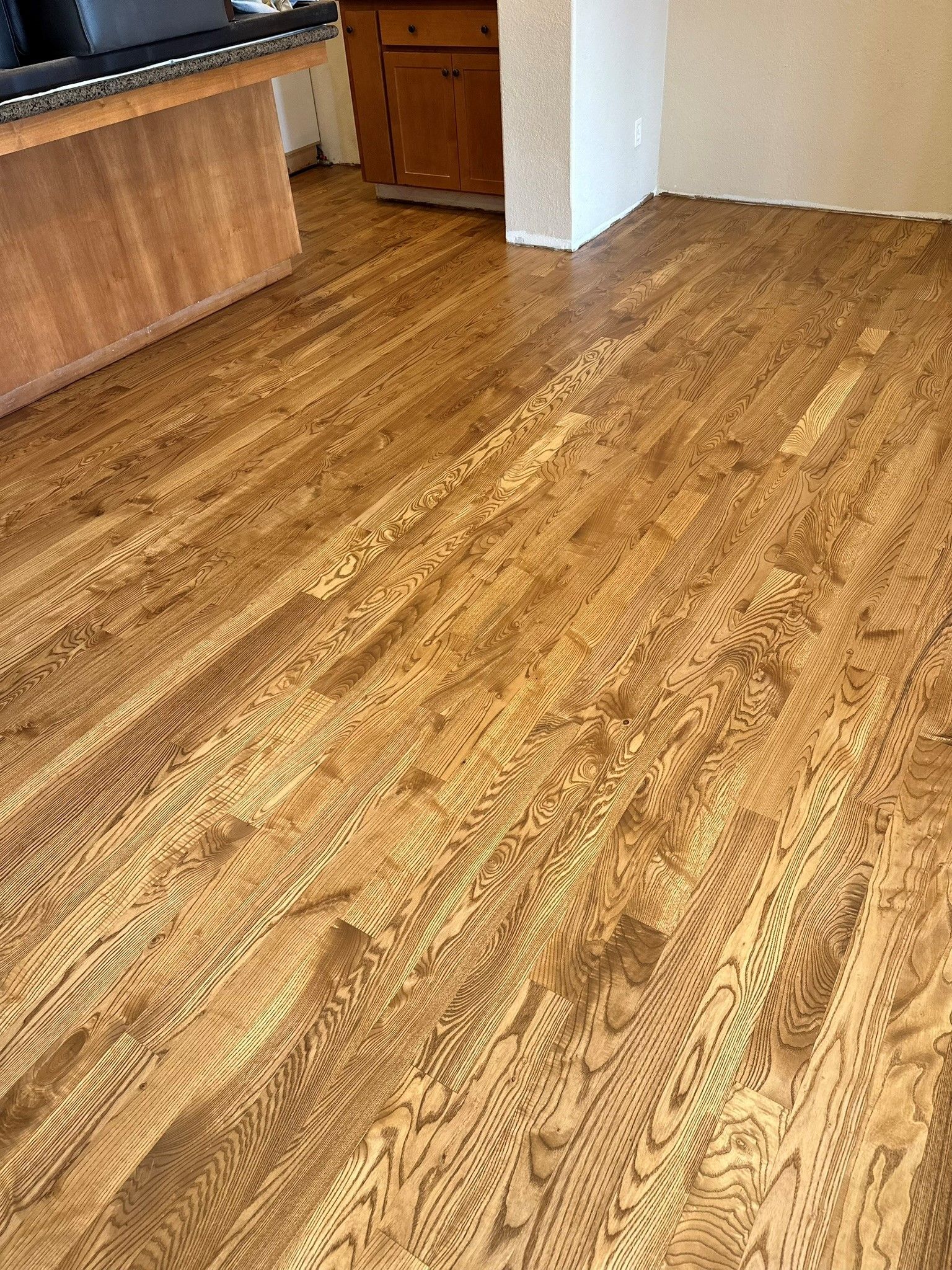A wooden floor in a room with a kitchen in the background.
