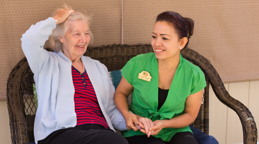 A woman in a green shirt is sitting next to an older woman on a wicker bench.