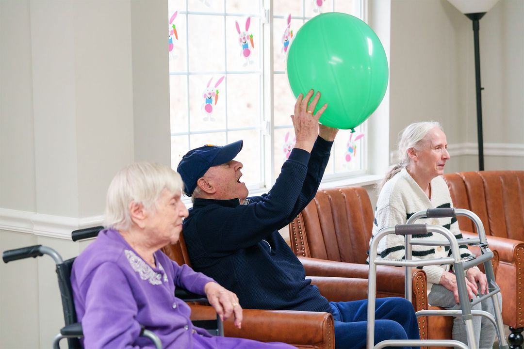 A group of elderly people are playing with a green balloon in a living room.