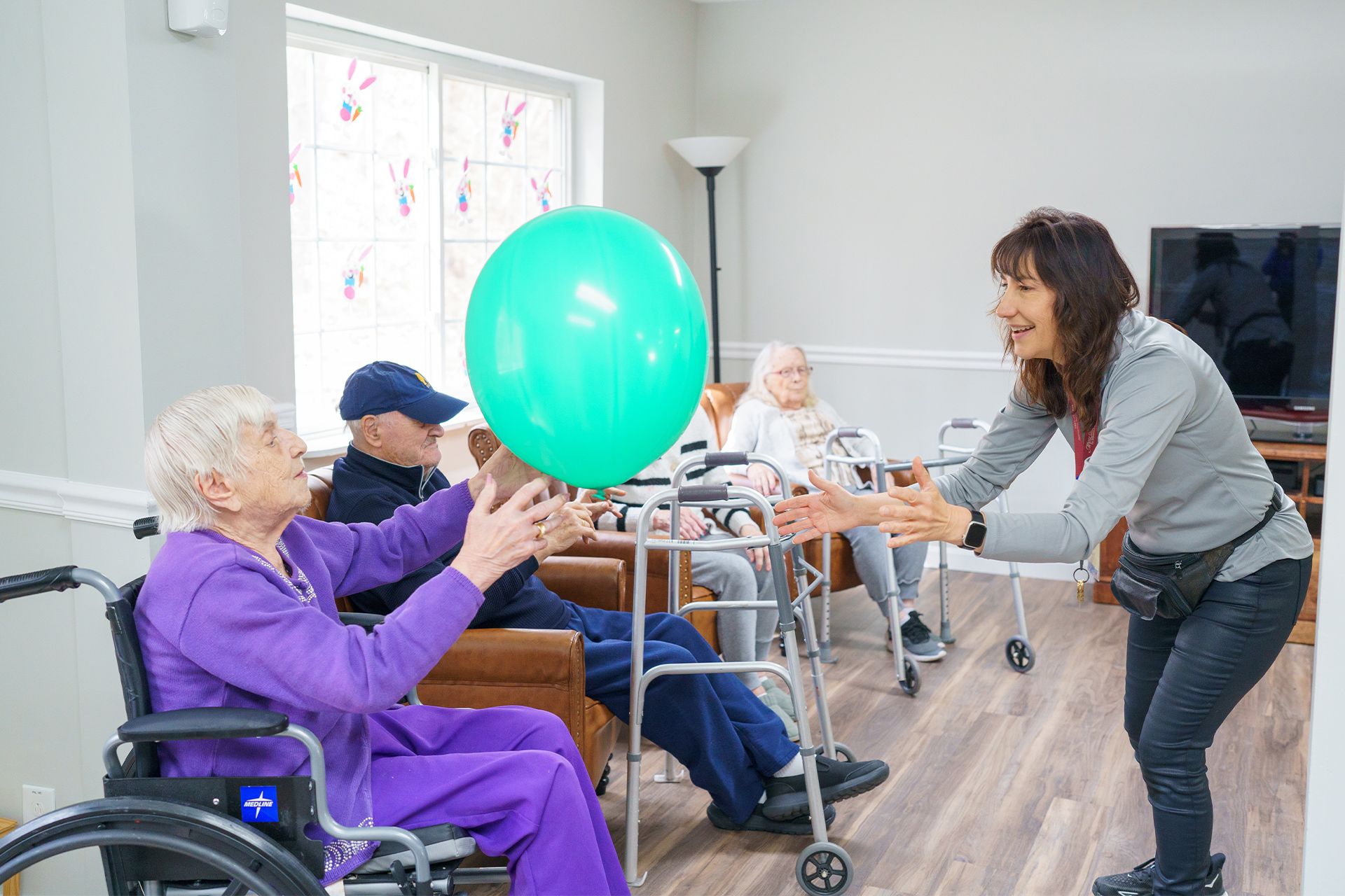 A woman is holding a green balloon in front of an elderly woman in a wheelchair.