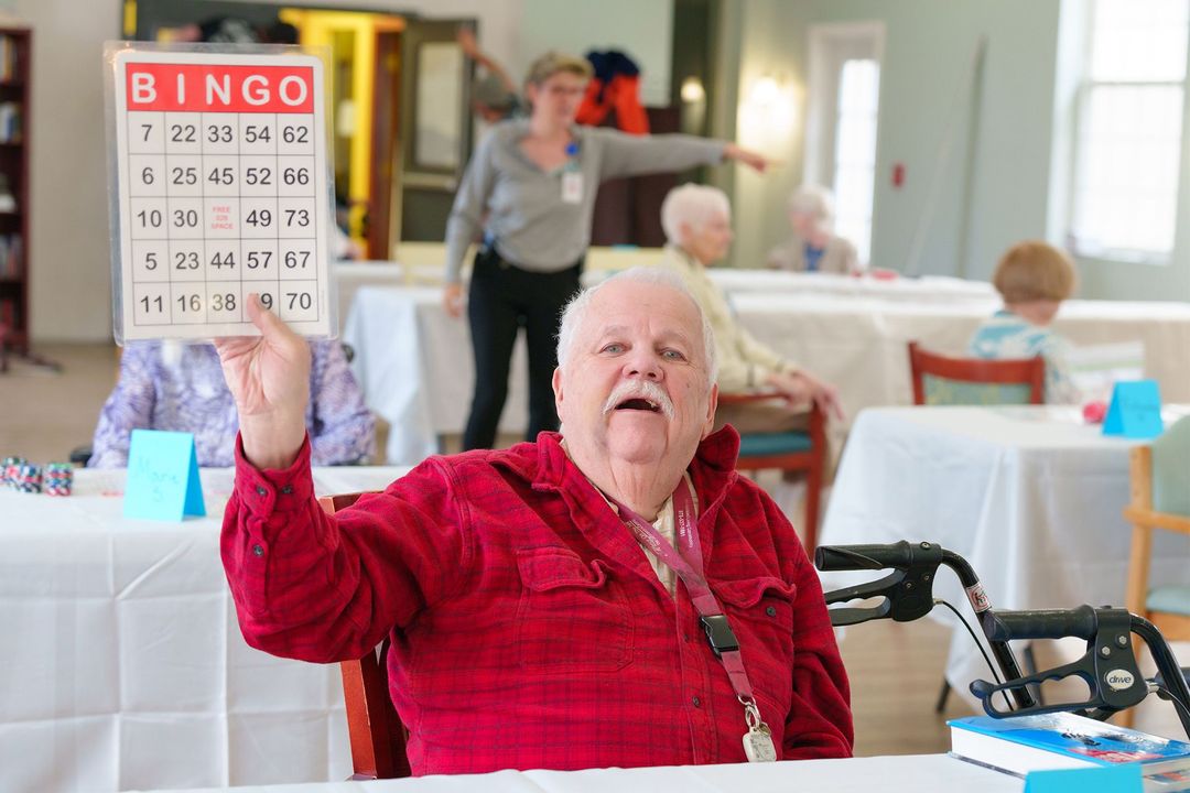 An elderly man is sitting at a table holding a bingo card.