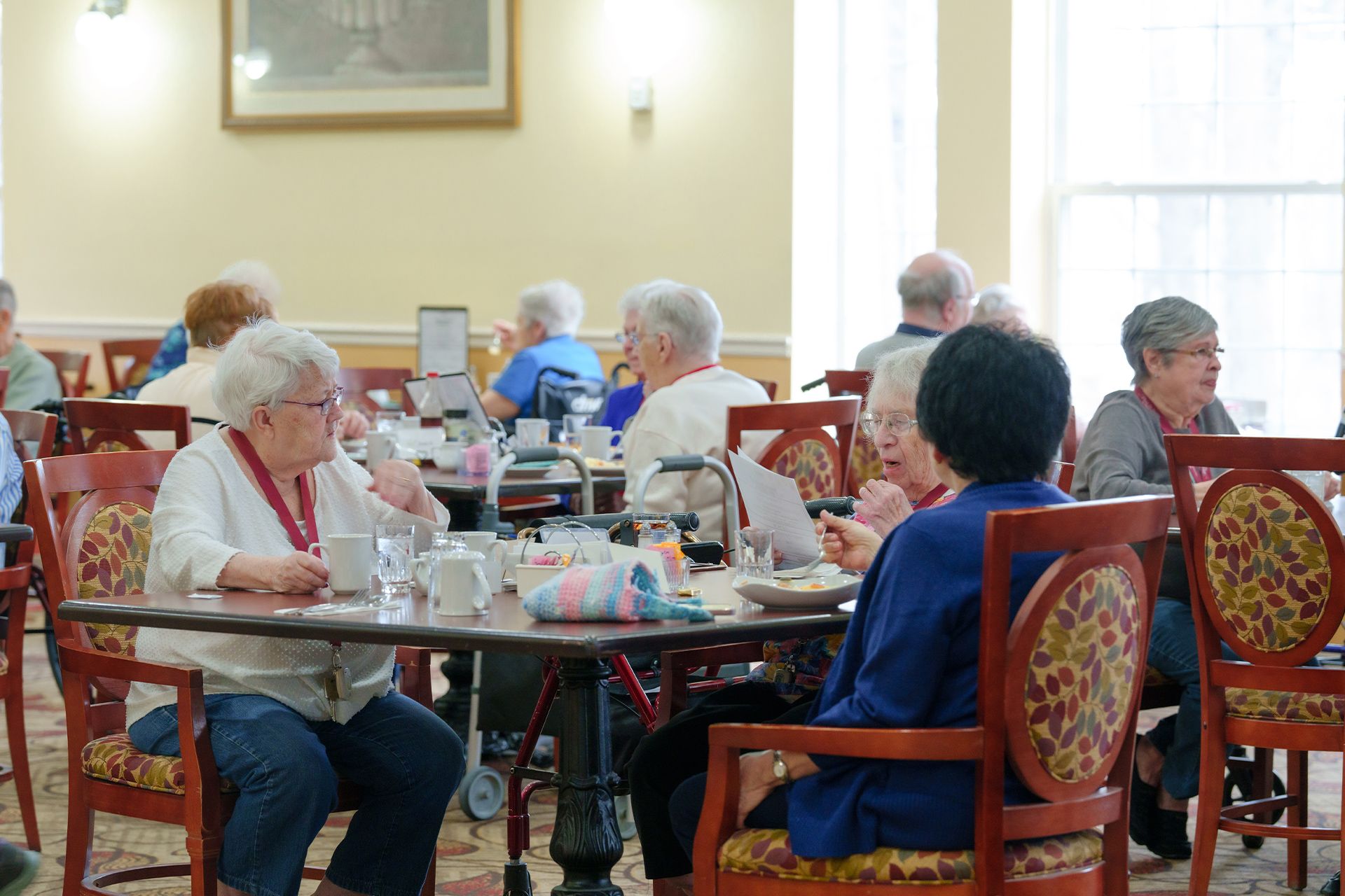 A group of elderly people are sitting at tables in a dining room.