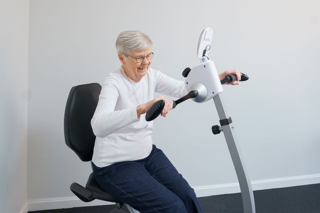 An elderly woman is riding an exercise bike in a room.