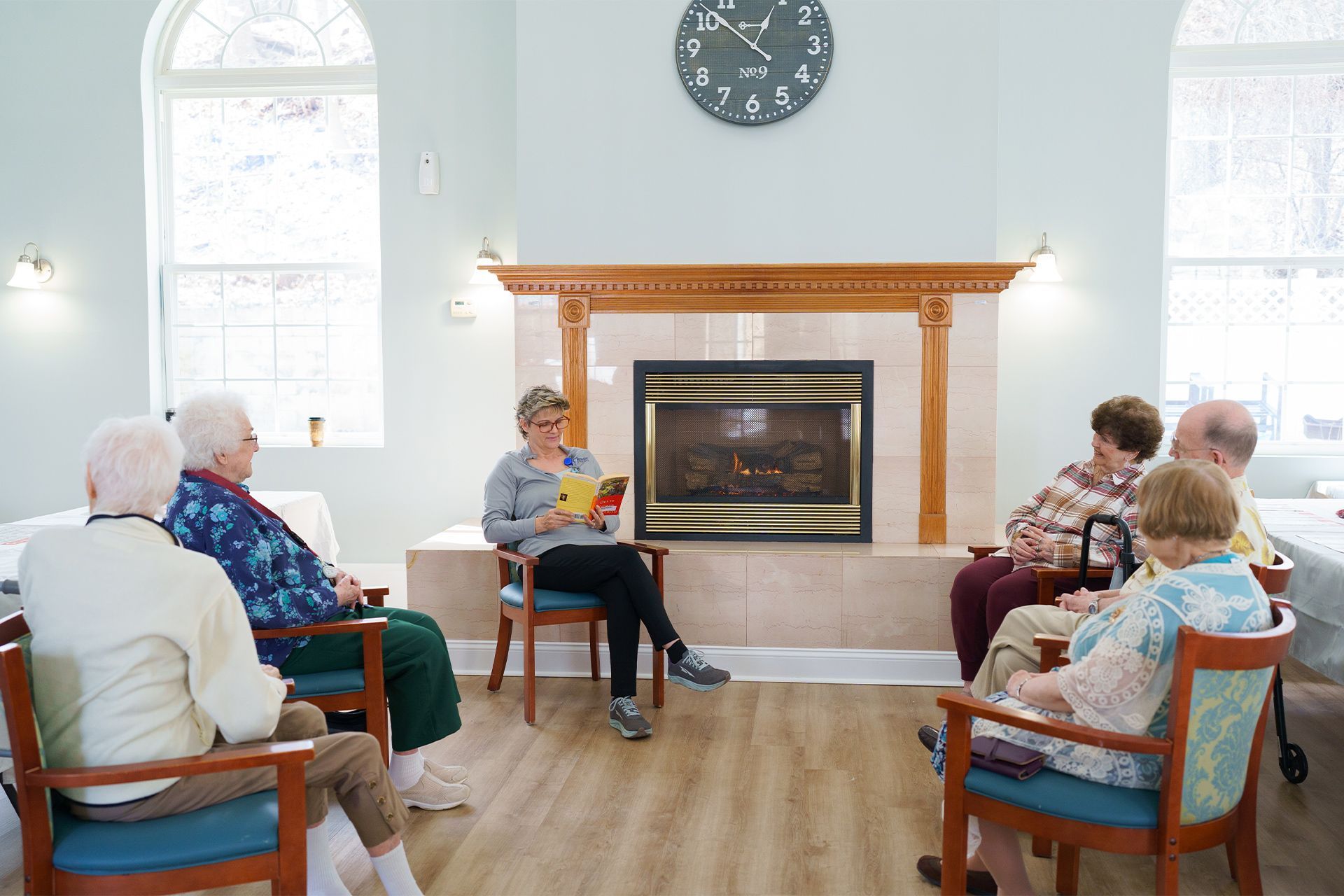 A group of elderly people are sitting in chairs in front of a fireplace.