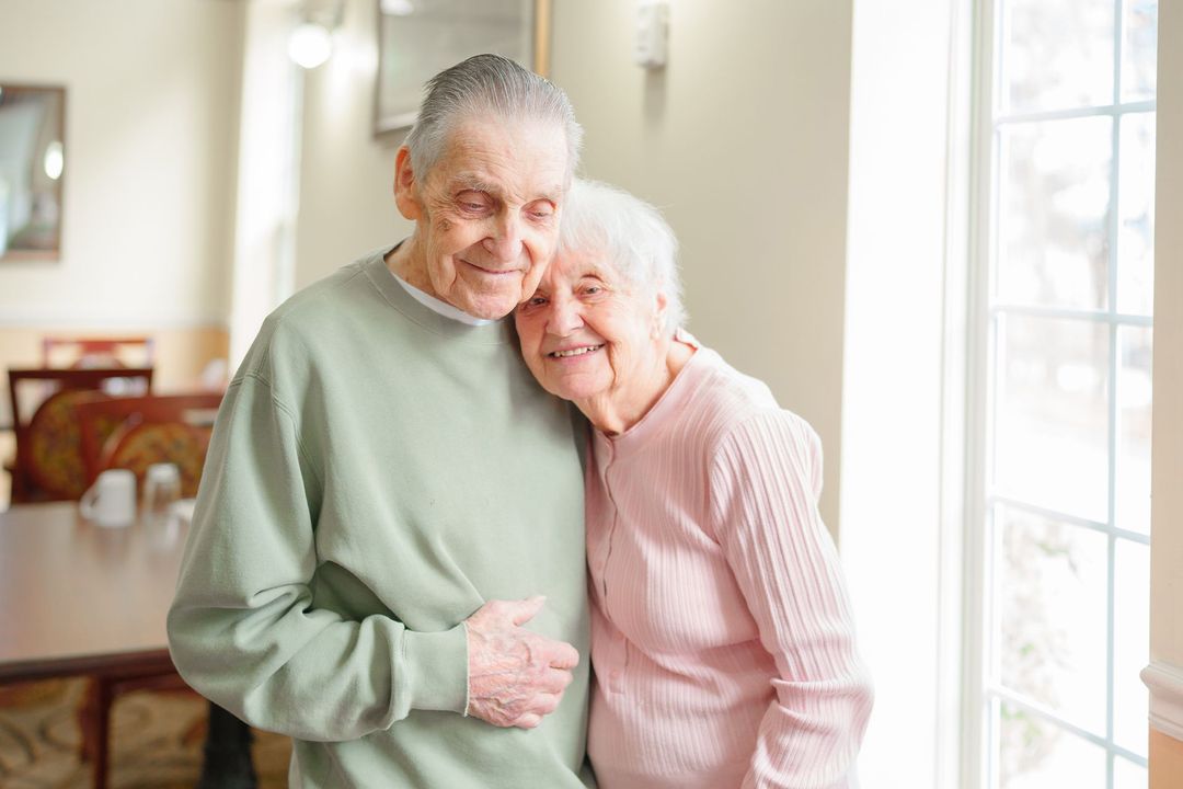 An elderly couple is standing next to each other in a room.