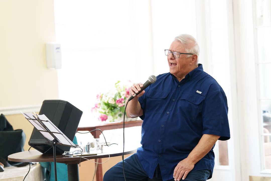 A man is singing into a microphone while sitting on a stool.