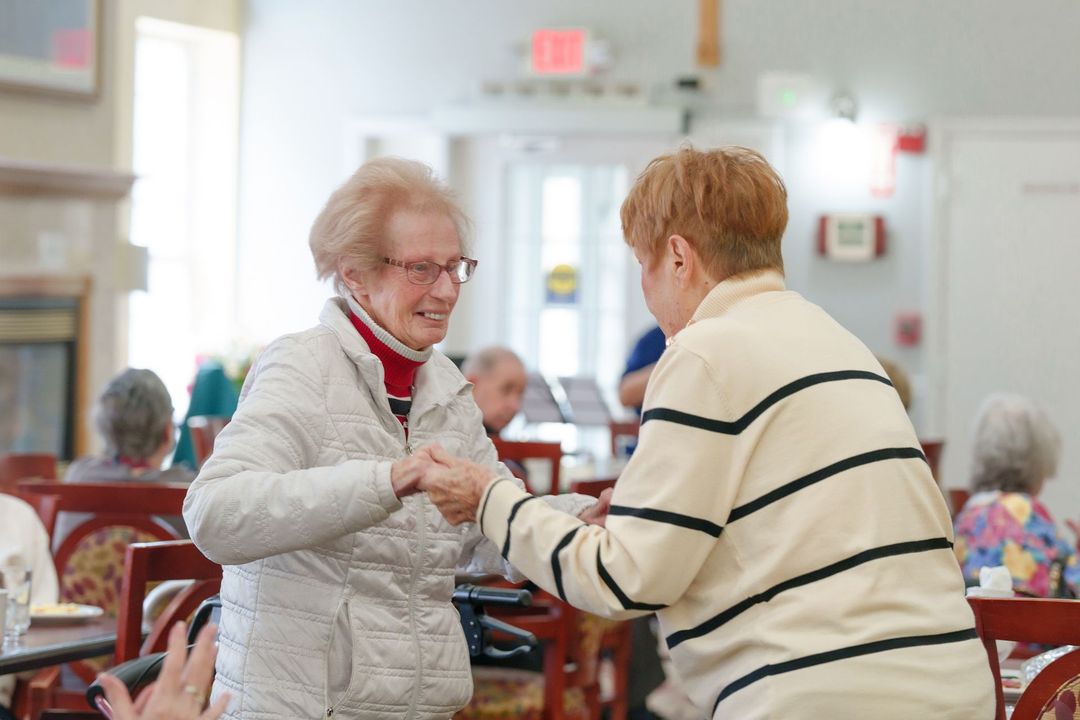 Two older women are dancing together in a nursing home.