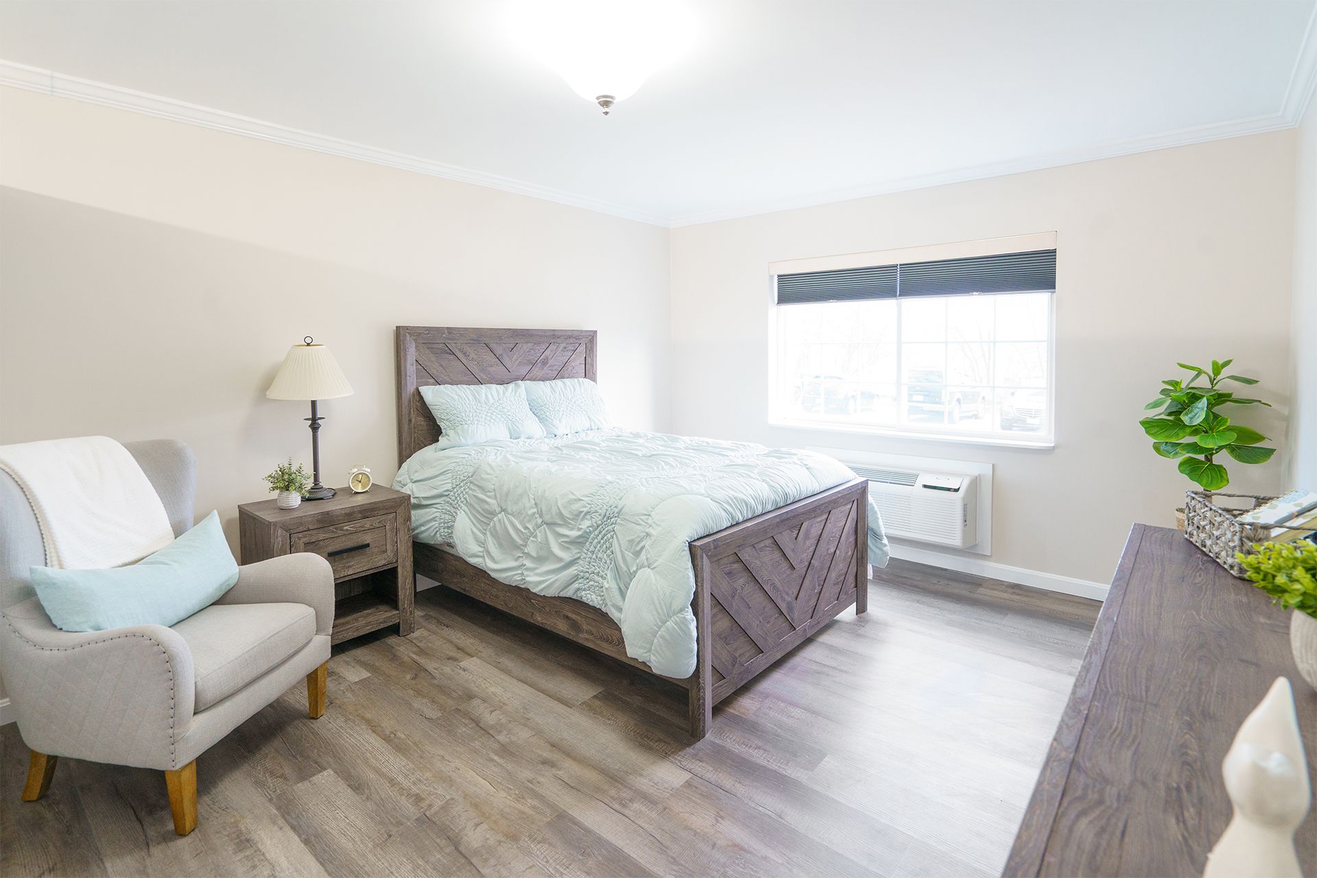 A bedroom with a bed , chair , nightstand and dresser.