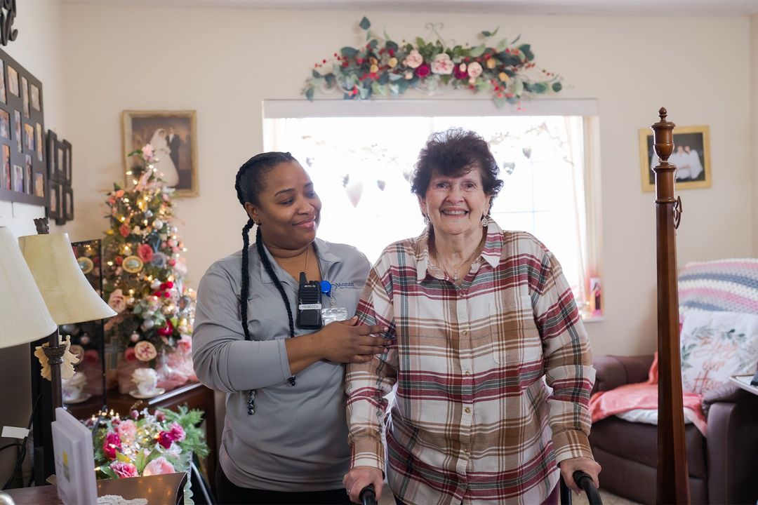 Two women are standing next to each other in a living room in front of a christmas tree.