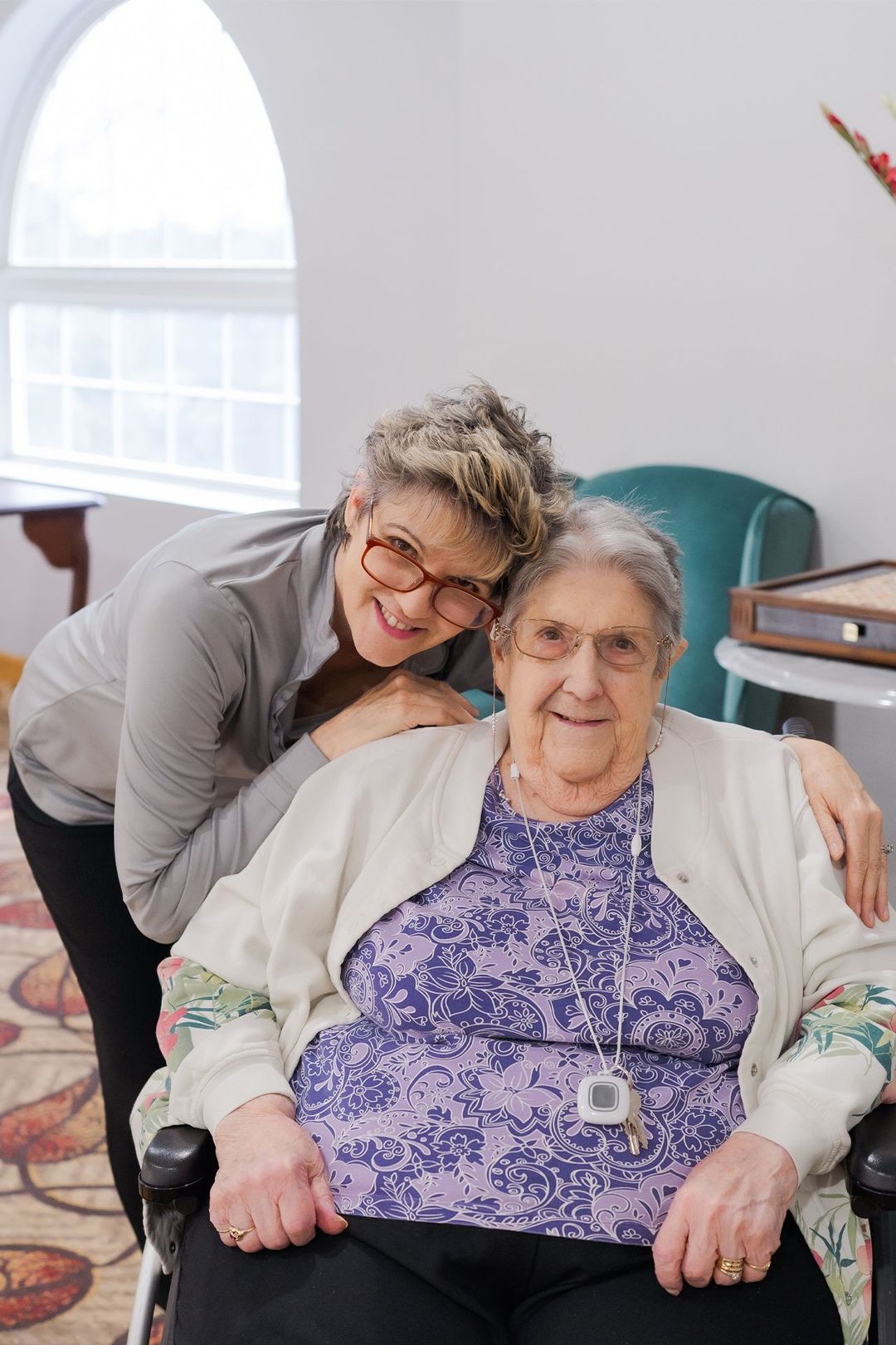 A woman is standing next to an elderly woman in a wheelchair.