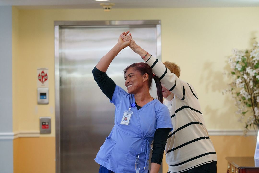 A nurse and a woman are dancing in front of an elevator.