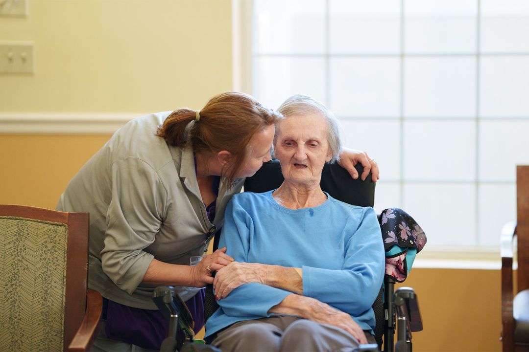 An elderly woman in a wheelchair is being comforted by a nurse.