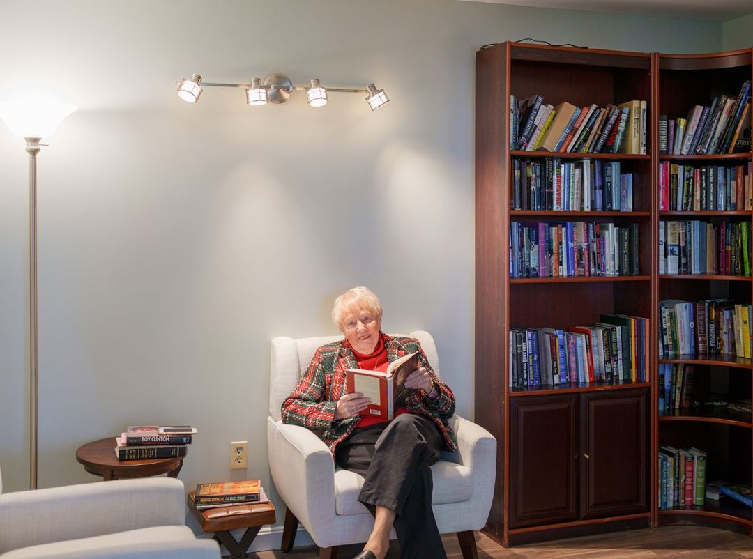 A woman is sitting in a chair reading a book in a library.