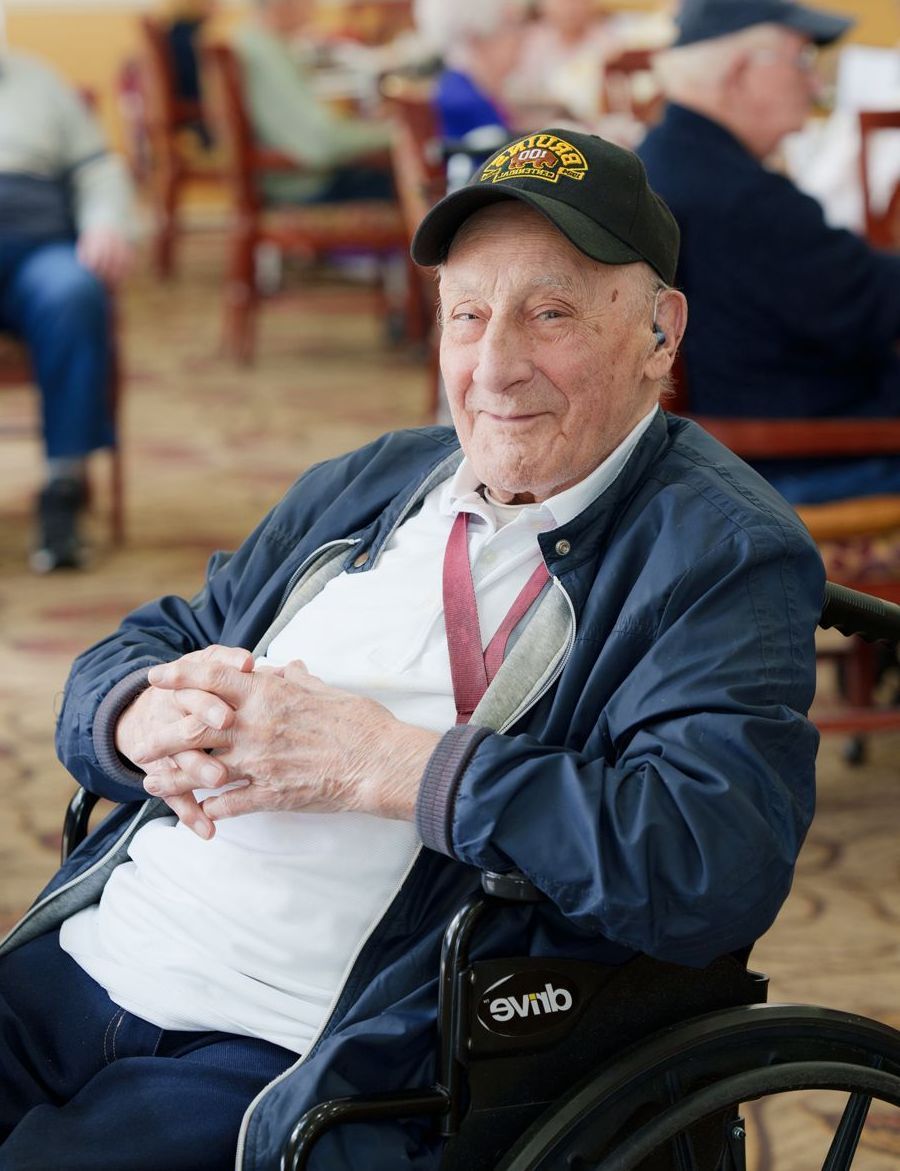 An elderly man is sitting in a wheelchair and wearing a hat.