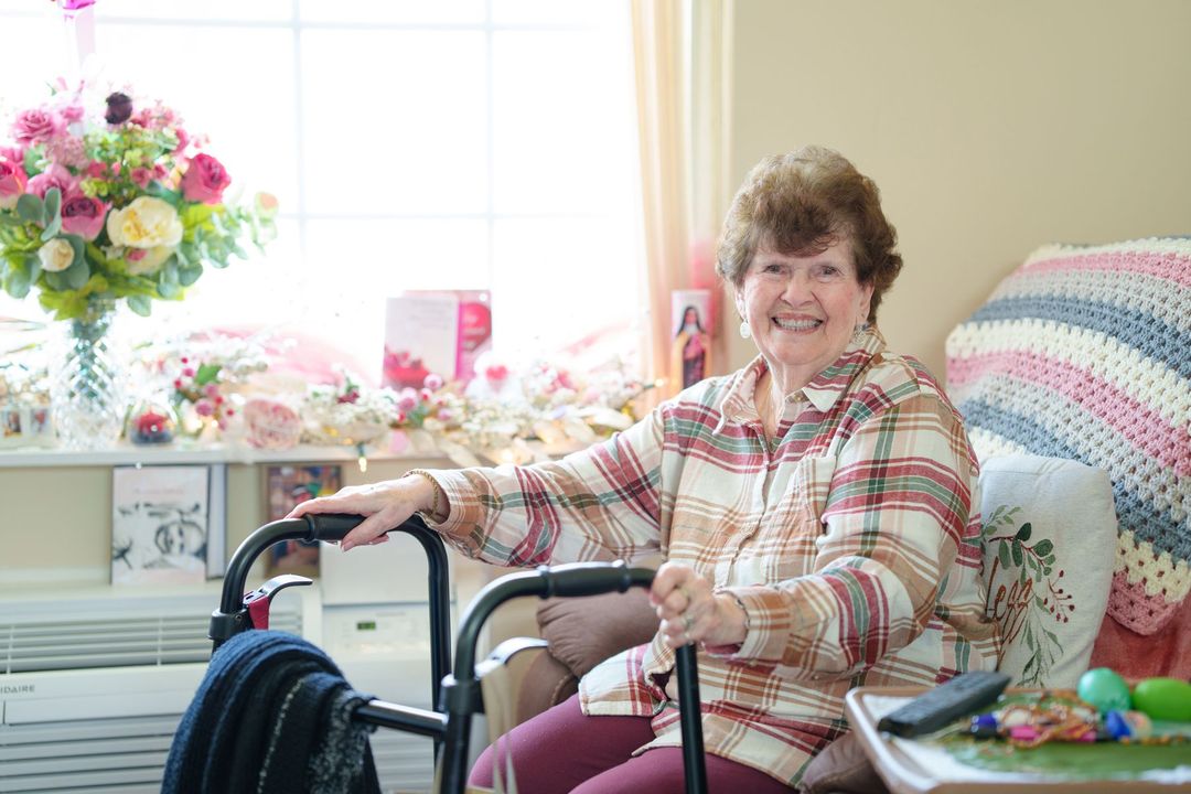 An elderly woman is sitting in a chair with a walker.