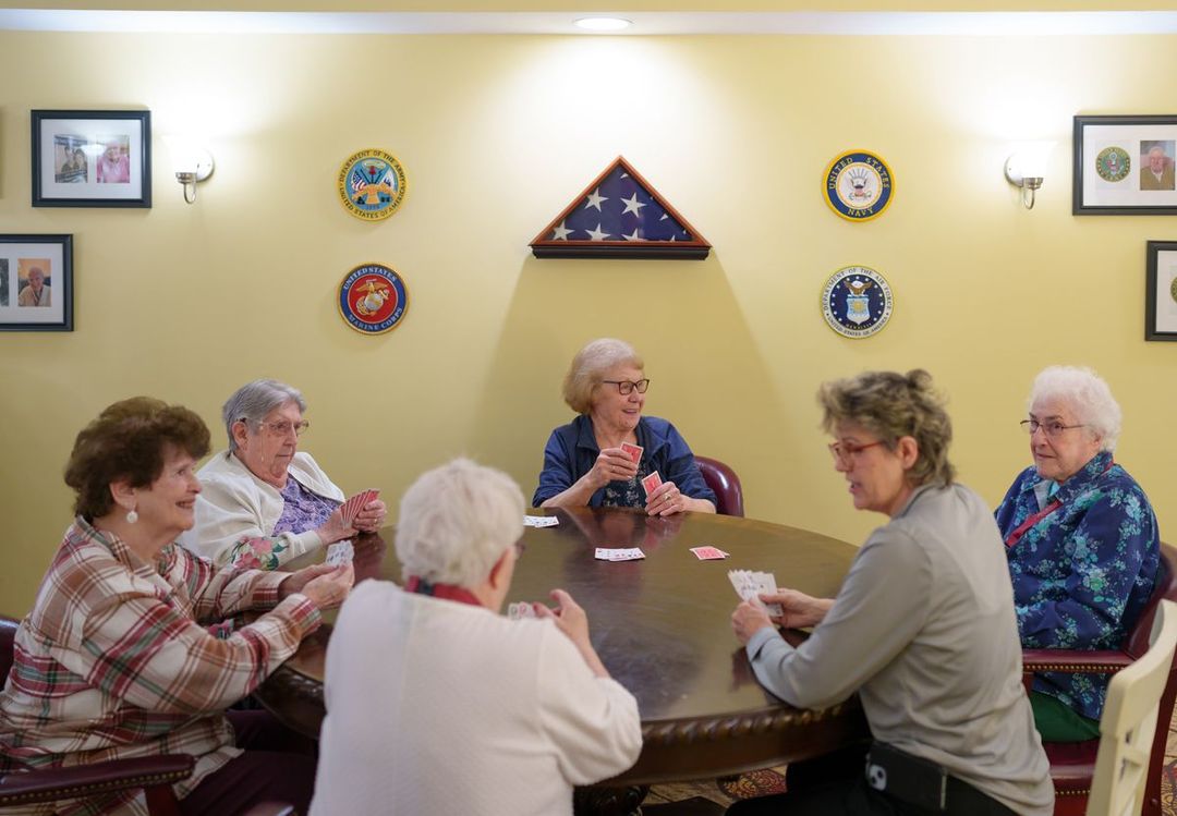 A group of elderly women are sitting around a table playing cards.