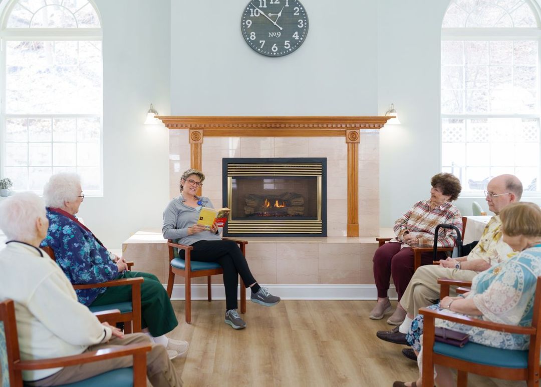 A group of elderly people are sitting around a fireplace in a living room.